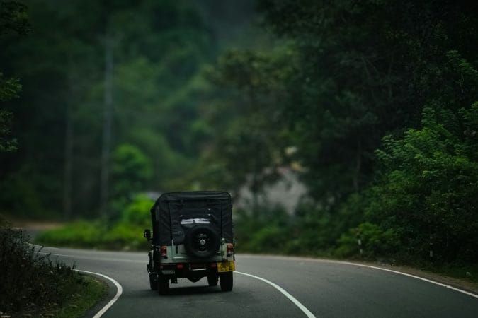 a jeep driving down a road in the middle of a forest