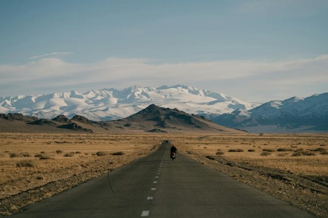 Snowy mountains behind asphalt road and hills