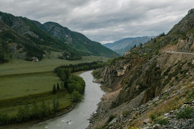 Picturesque view of rough mountain slope near stream and green vegetate under cloudy sky