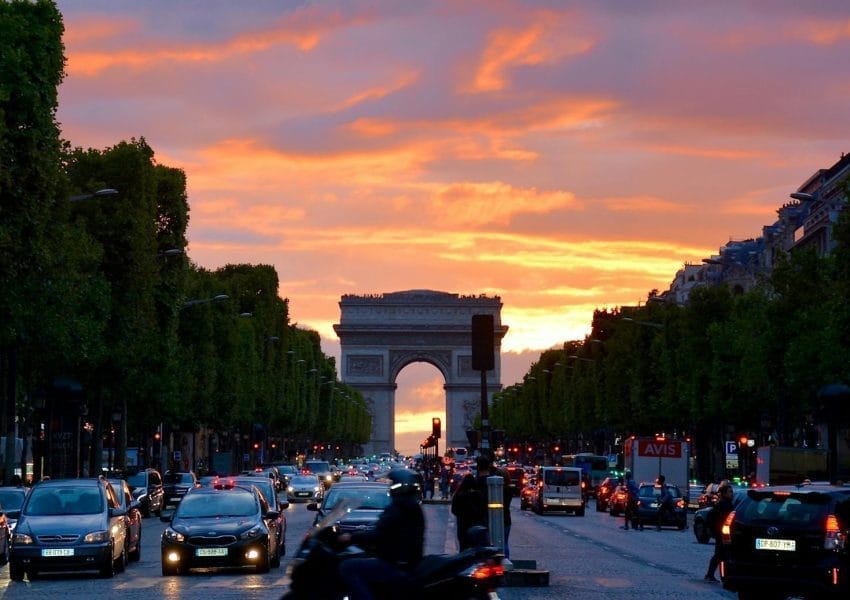 Vivid sunset sky over Arc de Triomphe, capturing Parisian traffic and architecture.